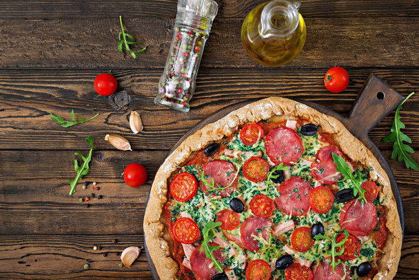 vista superior de la pizza con salami, tomates, aceitunas y queso sobre masa con harina de trigo integral
 - Foto, imagen
