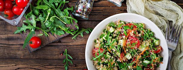 top view of salad with quinoa, arugula, radish, tomatoes and cucumbers in bowl on wooden background - Photo, Image