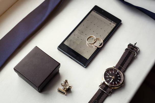 Different men's accessories such as: cufflinks, watches,  rings, belt, tie and phone - are on the table - 写真・画像