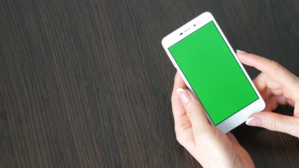Las manos femeninas con hermosa manicura francesa toman un teléfono inteligente blanco con pantalla verde. Usando Smartphone, sosteniendo Smartphone con pantalla verde en una elegante mesa de madera negra
 - Imágenes, Vídeo