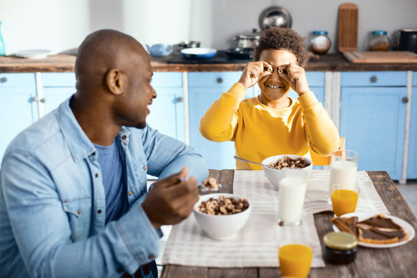 Upbeat pre-teen boy playing with cereals during breakfast - Foto, Imagem