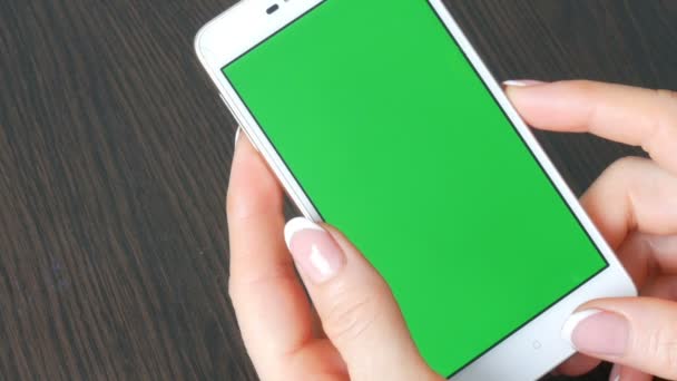 Női kezek gyönyörű francia manikűr vesz egy zöld képernyő fehér okostelefon. Használ Smartphone, gazdaság Smartphone-val egy elegáns fekete fából készült asztal Green Screen - Felvétel, videó