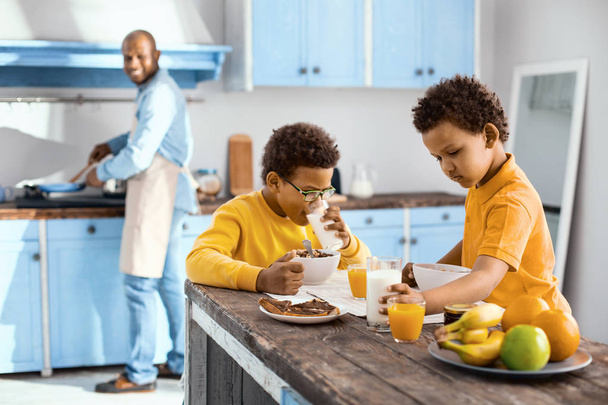 Pleasant children eating breakfast while their father cooking - Foto, Bild