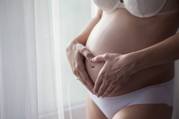 Живот беременной женщины в белых трусах, стоящей рядом с занавесками.
 - Фото, изображение