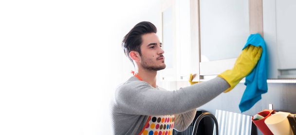 Young man in yellow gloves cleaning kitchen - Foto, Bild