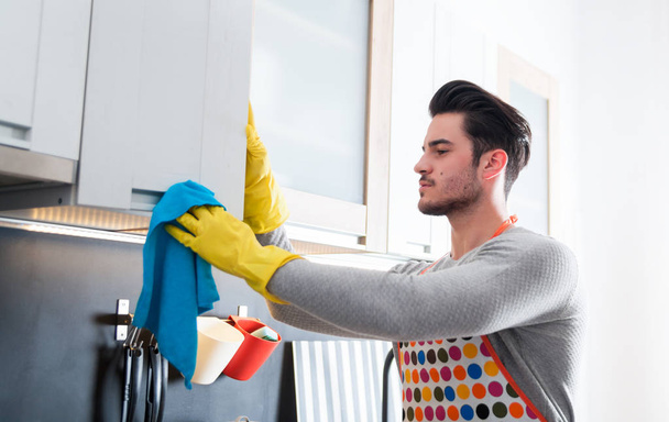 Young man in yellow gloves cleaning kitchen - Zdjęcie, obraz