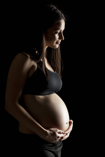 Silhouette of a beautiful pregnant woman on a black background - Foto, immagini