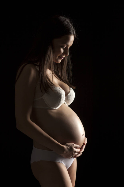 Silhouette of a beautiful pregnant woman in white underwear on a black background - Zdjęcie, obraz