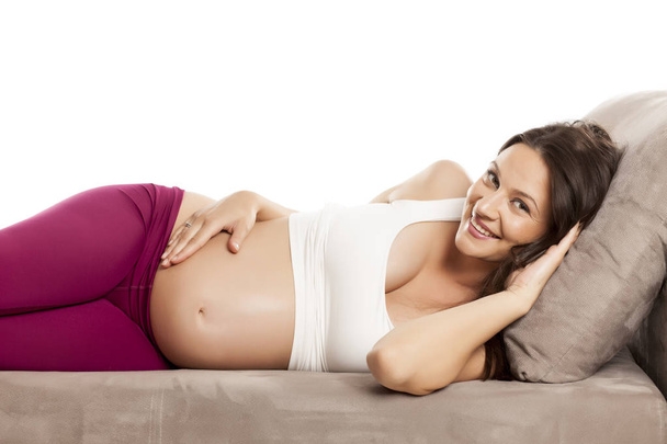 Happy beautiful pregnant woman lying on a bed on a white background  - Фото, изображение