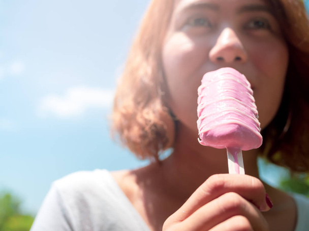 Mulher bonita cabelo curto vestindo camisa branca comendo rosa Popsicle Ice Pop derretendo em sua mão no fundo do céu azul verão
 - Foto, Imagem