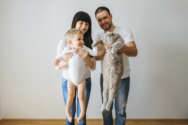 portrait of happy parents holding little toddler boy and grey cat at home - Фото, изображение