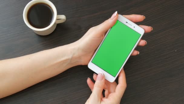 Női kezek gyönyörű francia manikűr vesz egy zöld képernyő fehér okostelefon közelében fehér csésze kávét. Használ Smartphone, gazdaság Smartphone-val egy elegáns fekete fából készült asztal Green Screen - Felvétel, videó