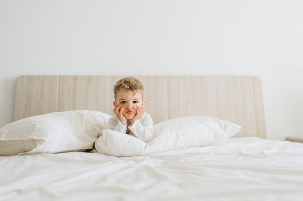 adorable toddler boy in white bodysuit lying on bed at home - Foto, imagen