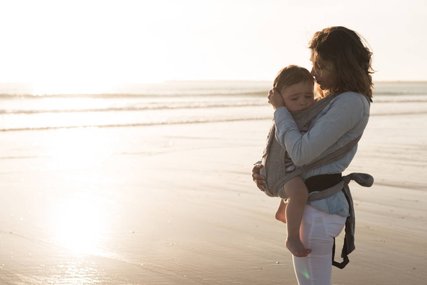 Mother with ergobaby carrying toddler on the beach - Photo, Image