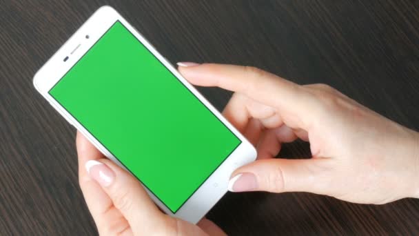 Ženské ruce s krásnou francouzskou manikúru si bílý smartphone s Green Screen. Pomocí Smartphone, držení Smartphone s Green Screen na stylový černý dřevěný stůl - Záběry, video