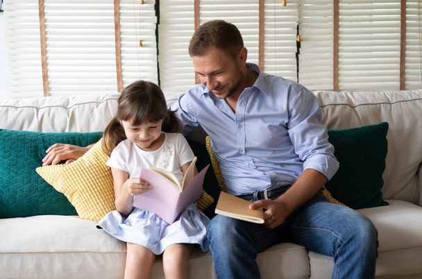Χρόνια μπαμπά γενεθλίων. Όμορφο κοριτσάκι με τον πατέρα της διαβάζοντας ένα βιβλίο στο σπίτι της. - Φωτογραφία, εικόνα