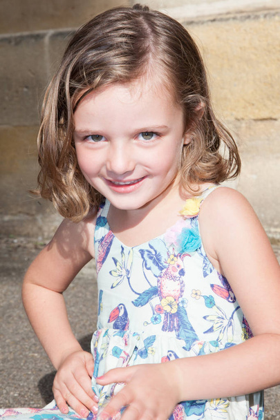 Портрет очаровательной улыбчивой маленькой девочки в платье на открытом воздухе в летний день
 - Фото, изображение