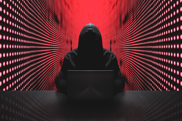Hacker anônimo na frente de seu computador com fundo de parede de luz vermelha
 - Foto, Imagem