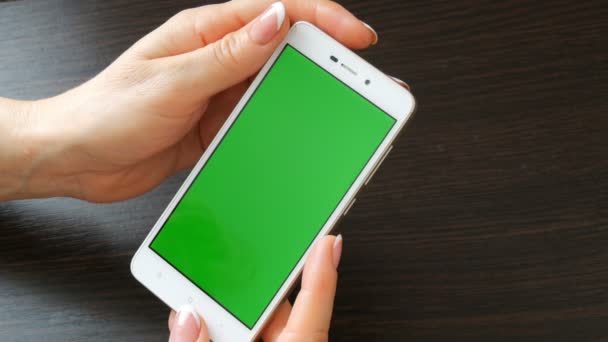 Γυναικεία χέρια με όμορφο γαλλικό μανικιούρ Πάρτε ένα λευκό smartphone με πράσινη οθόνη. Χρησιμοποιώντας το Smartphone, κρατώντας Smartphone με πράσινη οθόνη σε ένα κομψό μαύρο ξύλινο τραπέζι - Πλάνα, βίντεο