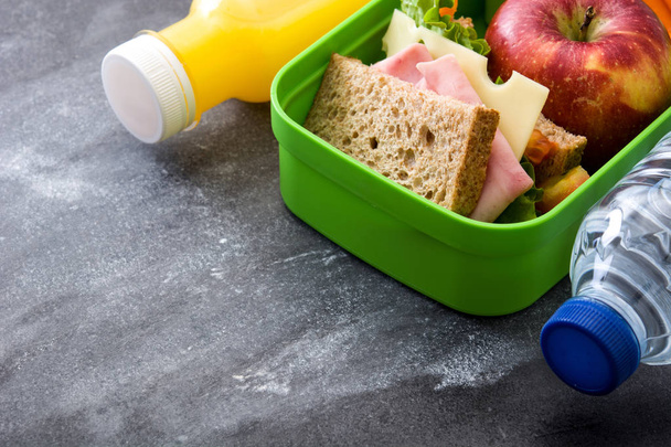 Egészséges iskolai ebéd-box: szendvics, a zöldség, a gyümölcs és a gyümölcslé a fekete kő. Szemközti nézet - Fotó, kép