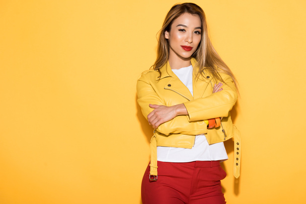 attractive young asian woman in leather jacket posing on yellow background  - Zdjęcie, obraz
