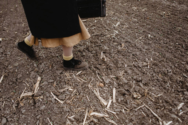 Χαμηλή τομή της γυναίκας στη φούστα με τα πόδια από το πεδίο σε κρύο καιρό - Φωτογραφία, εικόνα