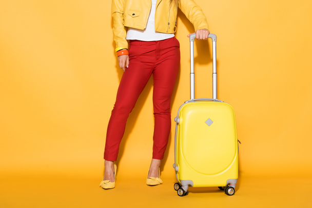 黄色の背景に動かされた袋の側に立ってスタイリッシュな女性旅行者のクロップ撮影 - 写真・画像