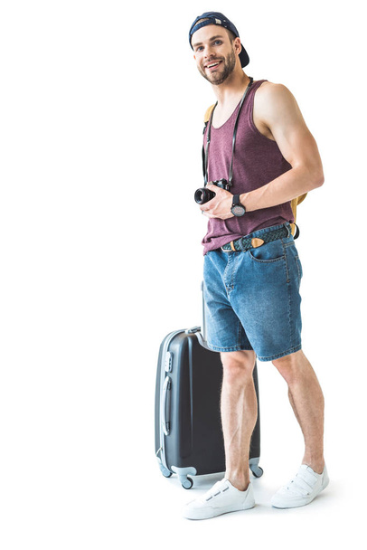 ευτυχισμένος αρσενικό τουριστικά με φωτογραφική μηχανή έτοιμη για το ταξίδι, που απομονώνονται σε λευκό και τσάντα ταξιδιού - Φωτογραφία, εικόνα