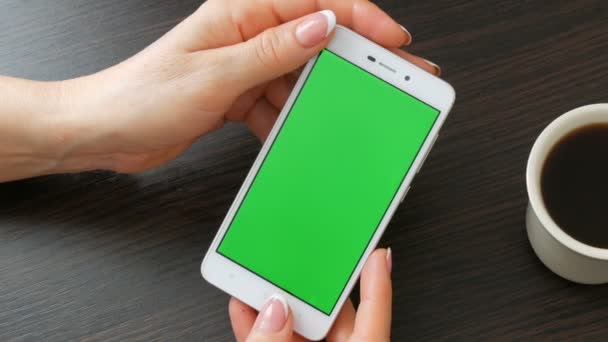 Női kezek gyönyörű francia manikűr vesz egy zöld képernyő fehér okostelefon közelében fehér csésze kávét. Használ Smartphone, gazdaság Smartphone-val egy elegáns fekete fából készült asztal Green Screen - Felvétel, videó