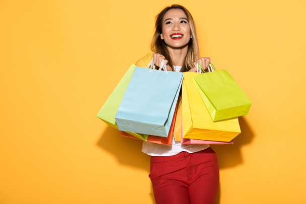 heureux shopper féminin debout avec des sacs en papier sur fond jaune
  - Photo, image