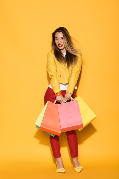 smiling asian woman with shopping bags on yellow background  - Photo, Image