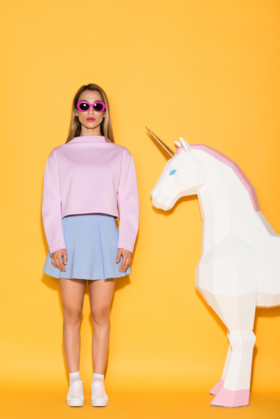 young stylish female model in sunglasses and decorative unicorn on yellow background  - Foto, afbeelding