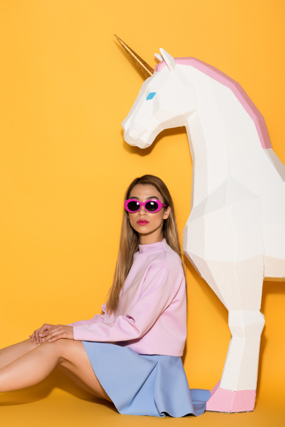 stylish asian female model in sunglasses and decorative unicorn on yellow background  - Fotografie, Obrázek