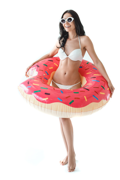 Lächelnde Frau im Bikini und Sonnenbrille mit aufblasbarem Donut, isoliert auf weiß - Foto, Bild