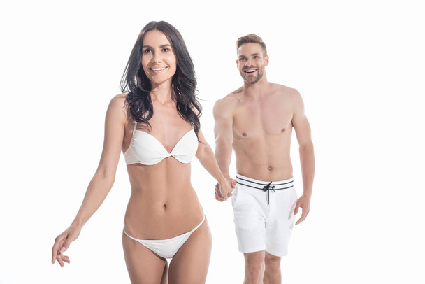 beautiful couple in swimwear holding hands and walking, isolated on white - Foto, Imagem