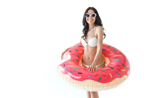 attraktive Frau im Bikini und Sonnenbrille posiert mit aufblasbarem Donut, isoliert auf weiß  - Foto, Bild