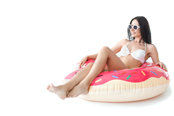 beautiful girl in bikini and sunglasses lying on inflatable donut, isolated on white - 写真・画像