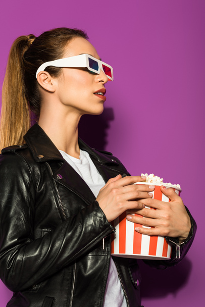 beautiful young woman in 3d glasses holding box of popcorn and looking away isolated on violet - Φωτογραφία, εικόνα