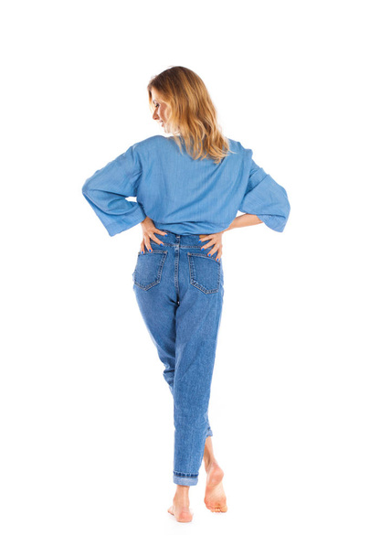 Back view jeans fashion. Full length portrait of young blonde woman in blue jeans standing isolated on a white background - Photo, image