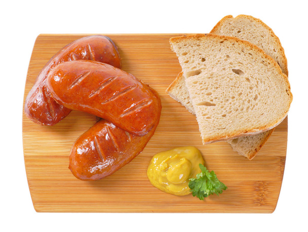 salchichas cortas y gruesas con rodajas de pan y mostaza sobre tabla de cortar de madera
 - Foto, imagen