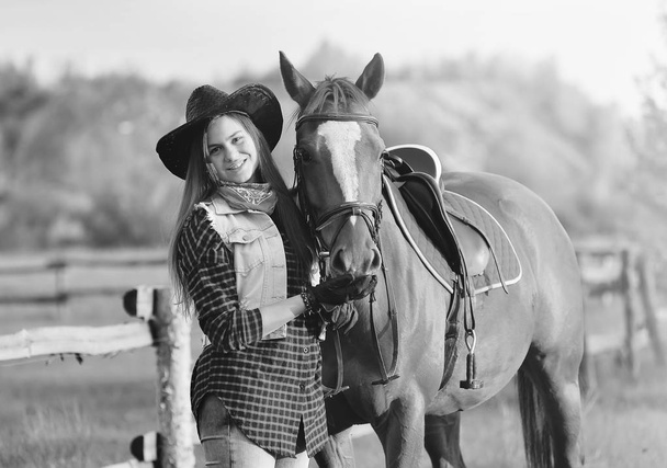 lehmityttö hatussa seisoo lähellä hevosta pellolla
 - Valokuva, kuva