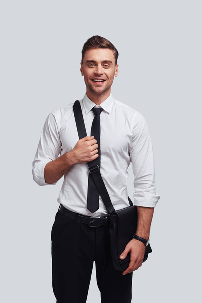 businessman carrying bag and smiling while standing against grey background - Foto, afbeelding