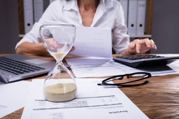 Close-up Of A Hourglass On Invoice In Front Of Businesswoman Working On Document - Foto, Bild