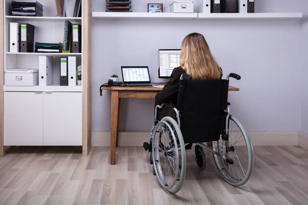 Rear View Of A Disabled Businesswoman Sitting On Wheelchair Working On Computer - Valokuva, kuva