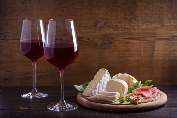 Weingläser mit Käse, Brot, Nüssen und Marmelade oder Prosciutto auf dunklem Holzgrund. Wein- und Essenskonzept - Foto, Bild