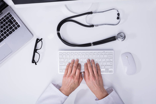 Elevated View Of A Doctor's Hand Typing On Computer Keyboard With Stethoscope On Desk - Foto, Bild