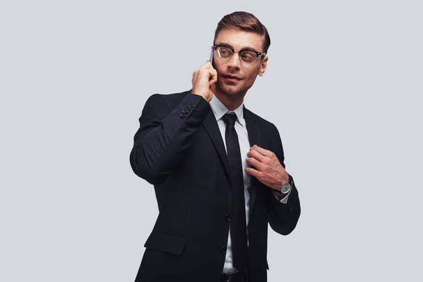 handsome young businessman talking on smart phone and looking away in studio  - Photo, image