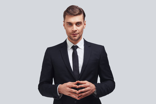 handsome young man in formal wear keeping hands clasped and looking at camera  - Foto, Bild