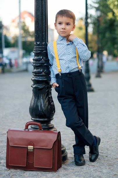 Niño posando en calle peatonal con maletín doblado
 - Foto, Imagen