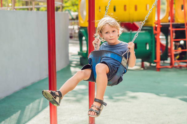 Funny kid boy having fun with chain swing on outdoor playground.  - Foto, Bild
